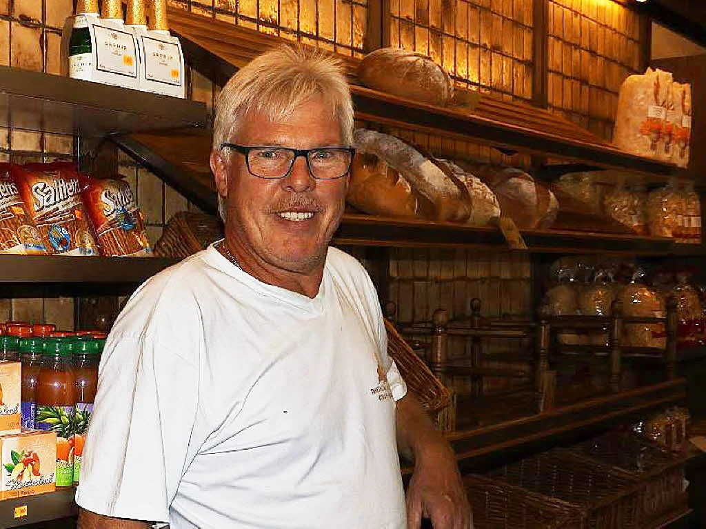 Lächelnder Mann mit Brille und weißem T-Shirt vor einem Brotregal