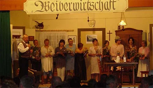 Theaterszene auf einer Bühne unter dem Schild „Weiberwirtschaft“