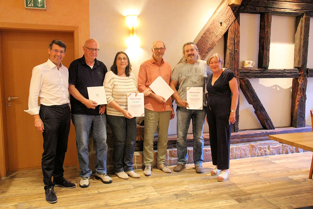 Sechs Personen mit Urkunden in einem Raum mit Fachwerk