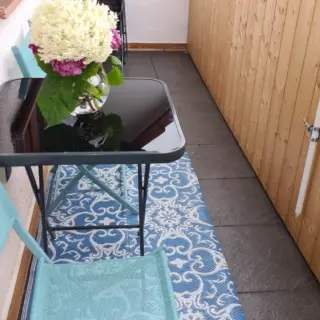Balkon mit Glastisch, Blumenstrauß und blauem Teppich