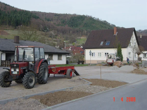 Traktor mit rotem Anhänger auf einer Baustelle am Festplatz, dahinter Wohnhäuser