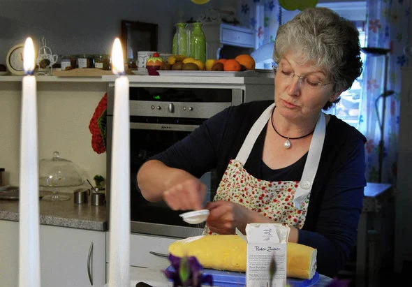 Frau mit Schürze richtet einen Kuchen an, davor stehen zwei brennende Kerzen