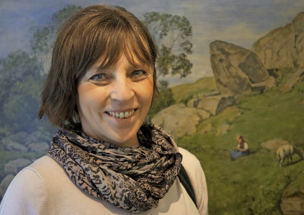 Lächelnde Frau mit gemustertem Schal vor einem Landschaftsgemälde