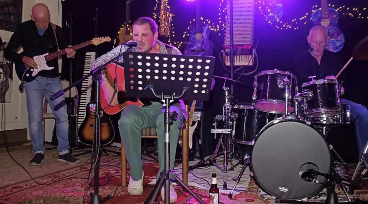 Sänger mit Gitarre auf einer Bühne mit Schlagzeug und Notenständer