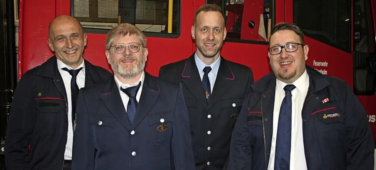 Drei Feuerwehrmänner in Uniform vor einem Feuerwehrfahrzeug