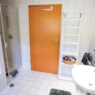 Badezimmer mit Dusche, Waschbecken und Holztür
