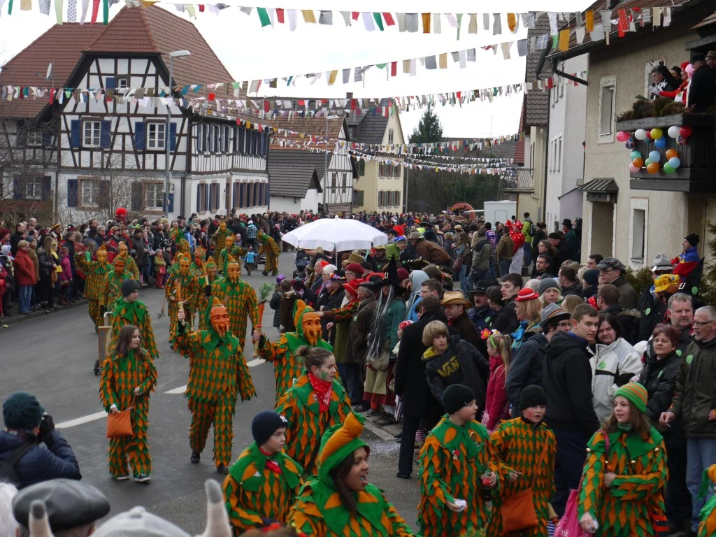 Narren in grün-orangen Kostümen und Zuschauer auf der Hauptstraße beim Umzug