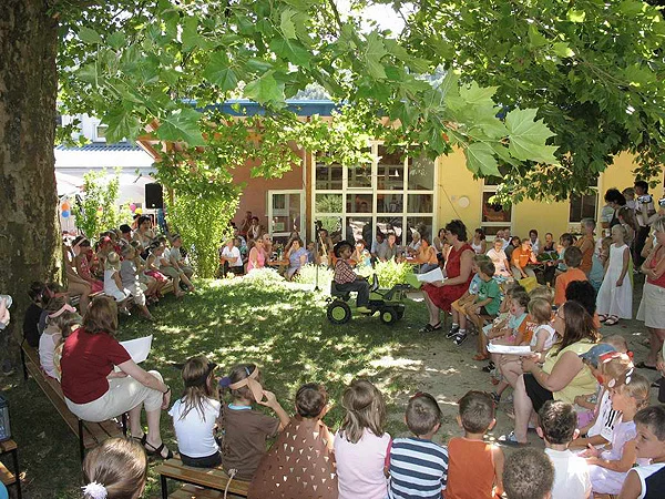 Kindergartenfest im Schatten großer Bäume mit vielen Zuschauenden