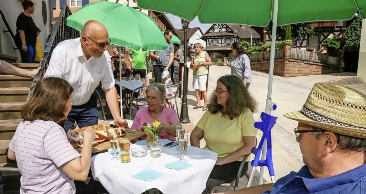 Gäste sitzen bei Sonnenschein unter einem grünen Sonnenschirm auf einer Terrasse