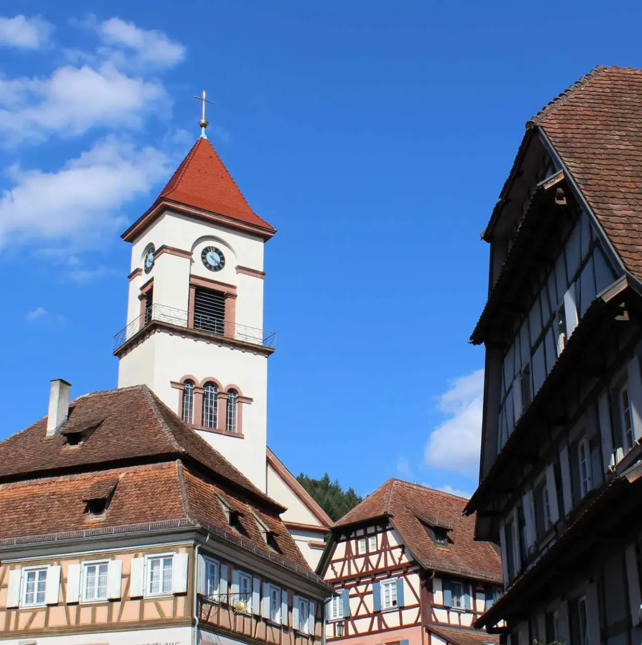 Kirchturm mit rotem Dach zwischen Fachwerkhäusern vor blauem Himmel