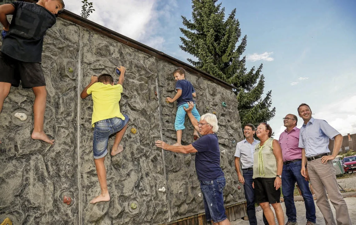 Kinder klettern an einer Kletterwand, daneben stehen Erwachsene