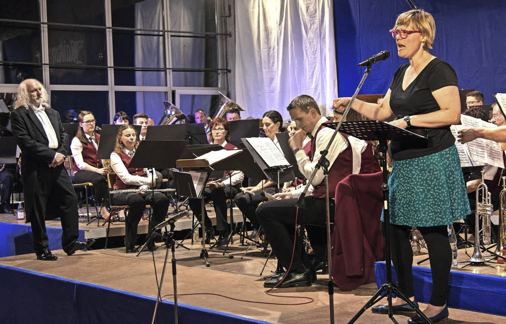 Frau am Mikrofon vor einem Orchester auf der Bühne
