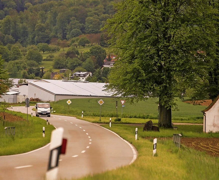 Kurvige Landstraße zwischen Wiesen und Wald mit einer großen Halle