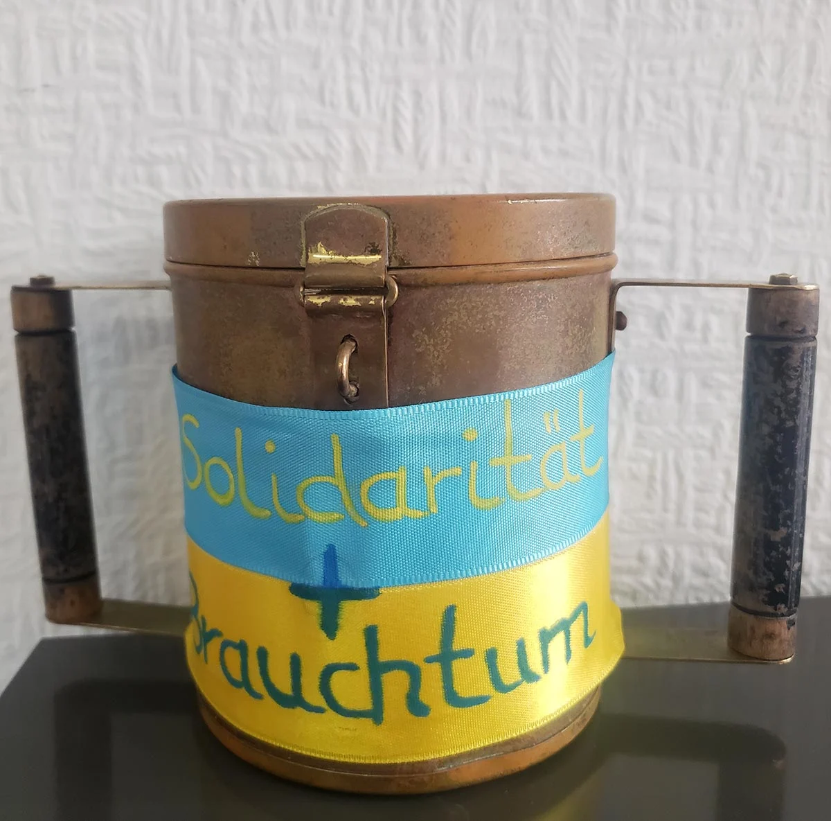 Sammelbüchse mit blau-gelber Schleife und der Aufschrift „Solidarität und Brauchtum“