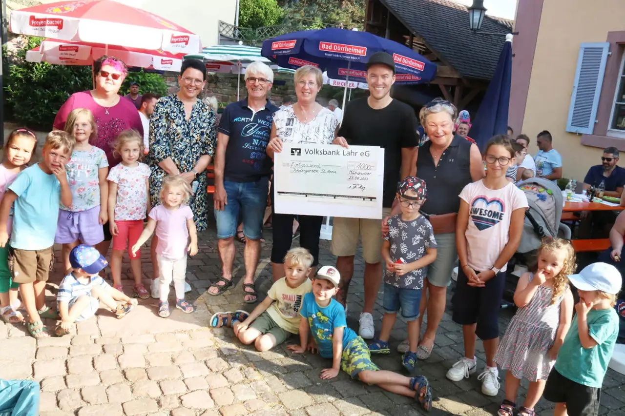 Erwachsene und Kinder mit einem großen Spendenscheck auf einem Dorfplatz