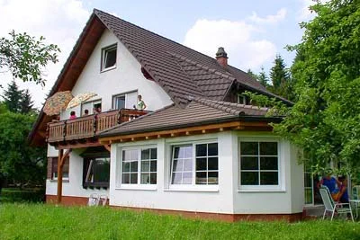 Haus mit Balkon und Anbau mit großen Fenstern, davor eine Wiese