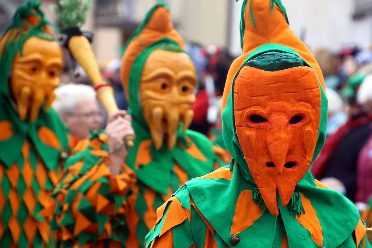 Narren in grün-orangen Kostümen mit Karottenmasken beim Umzug