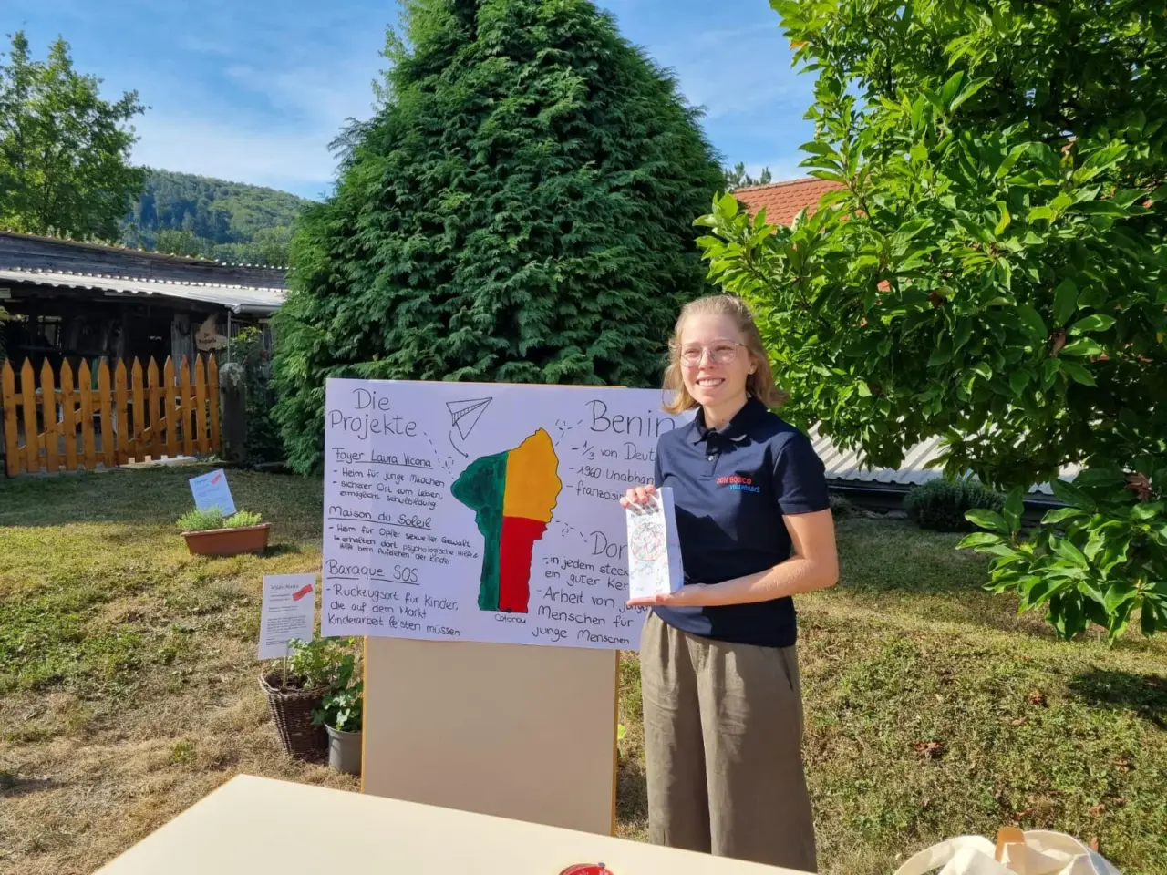 Junge Frau neben einem selbstgemachten Plakat mit der Flagge von Benin im Garten