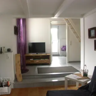 Wohnraum mit Fernseher, Sofa und offener Treppe